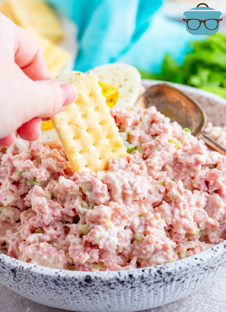 a person dipping crackers into a bowl of tuna salad