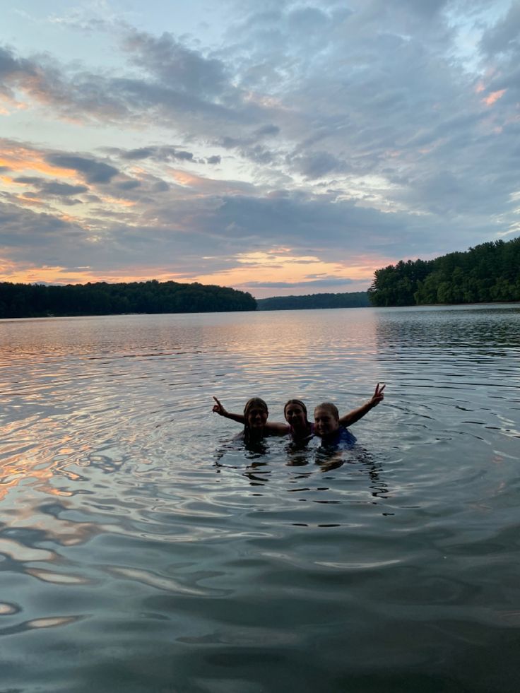 two people are swimming in the water at sunset