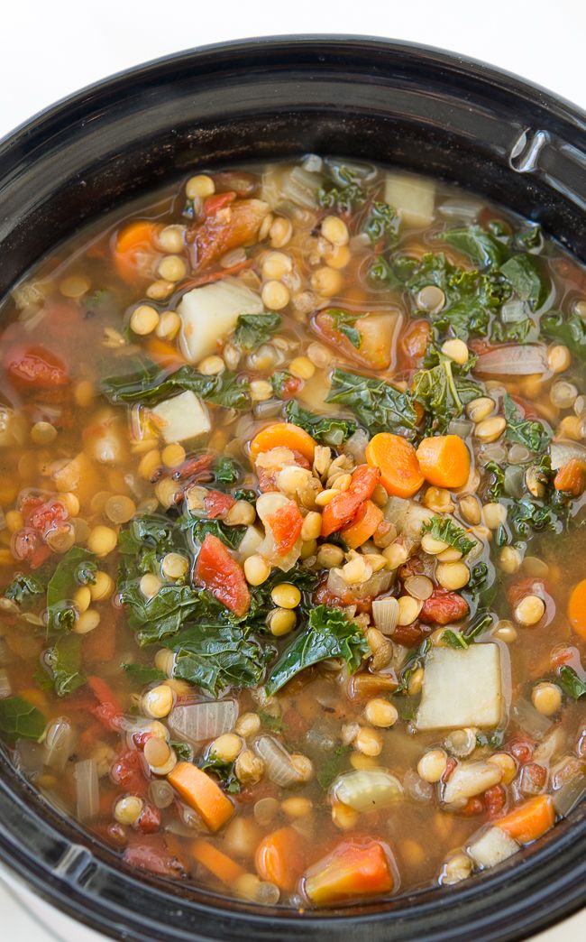 a black crock pot filled with soup and vegetables on top of a white table