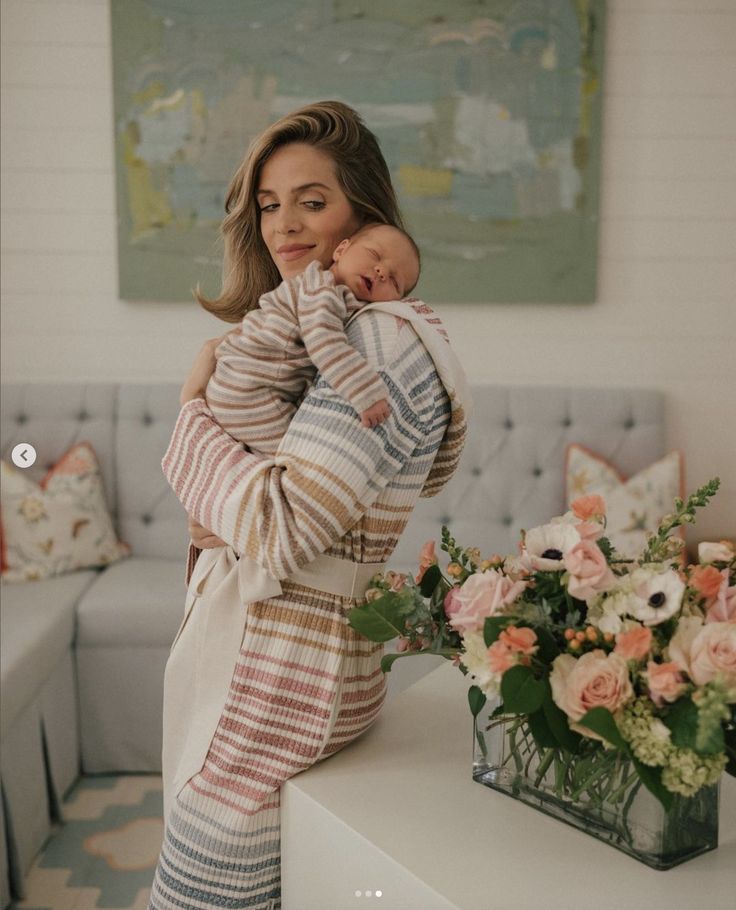 a woman holding a baby in her arms while standing next to a table with flowers