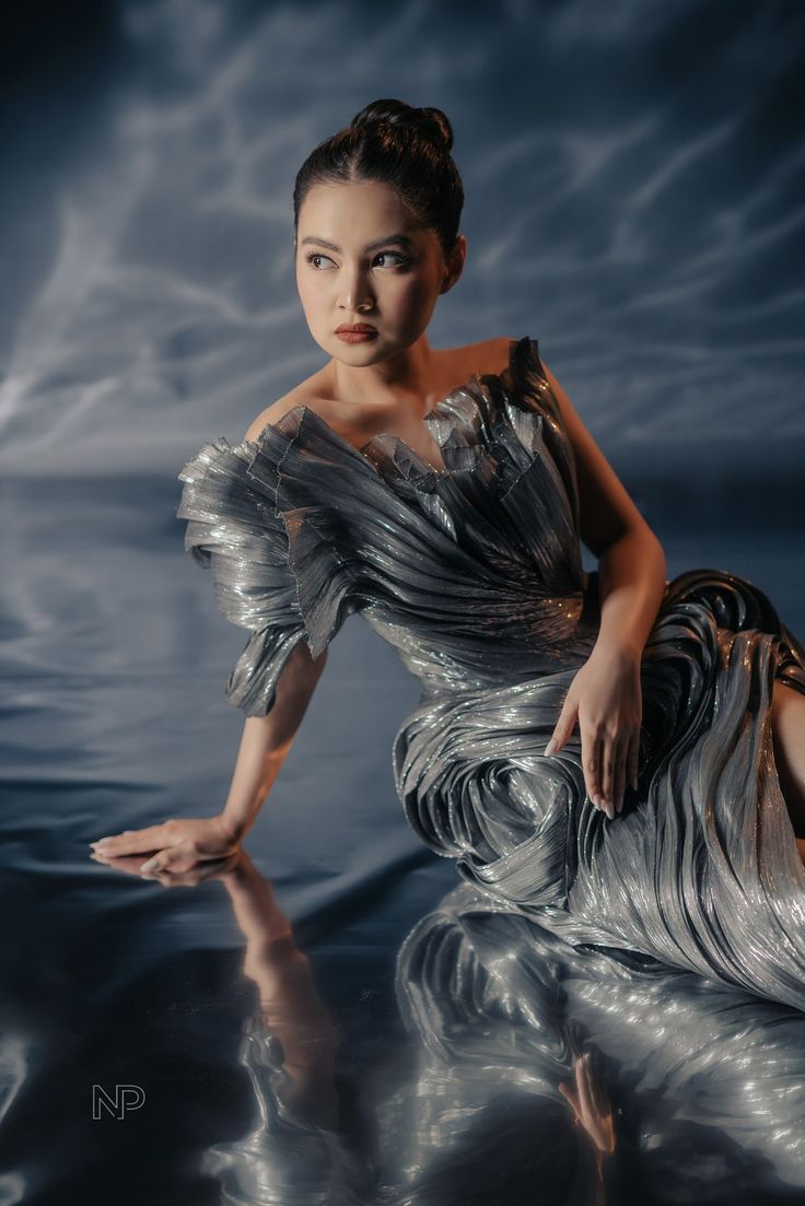 a woman in a silver dress is sitting on the water with her legs spread out