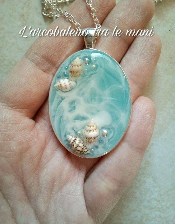 a hand holding a glass pendant with shells in the ocean on it's side