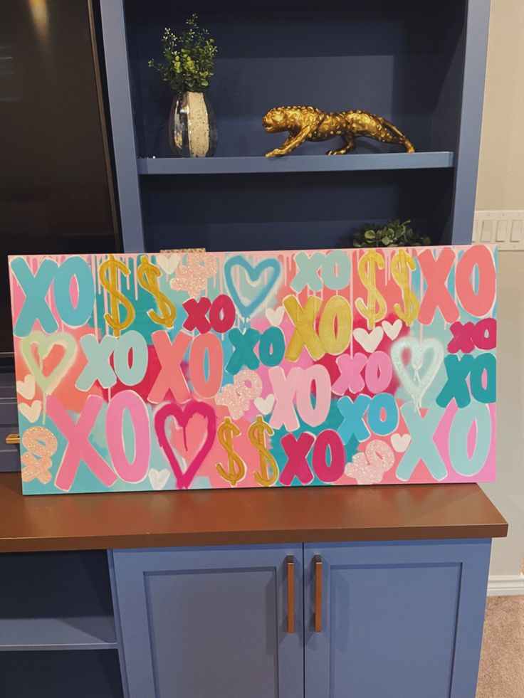 a painted sign on top of a blue cabinet in front of a bookcase with books