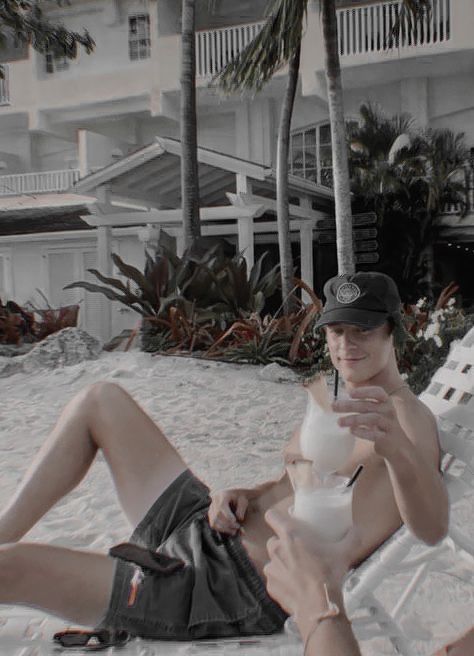 a man sitting on the beach with a drink in his hand and palm trees behind him