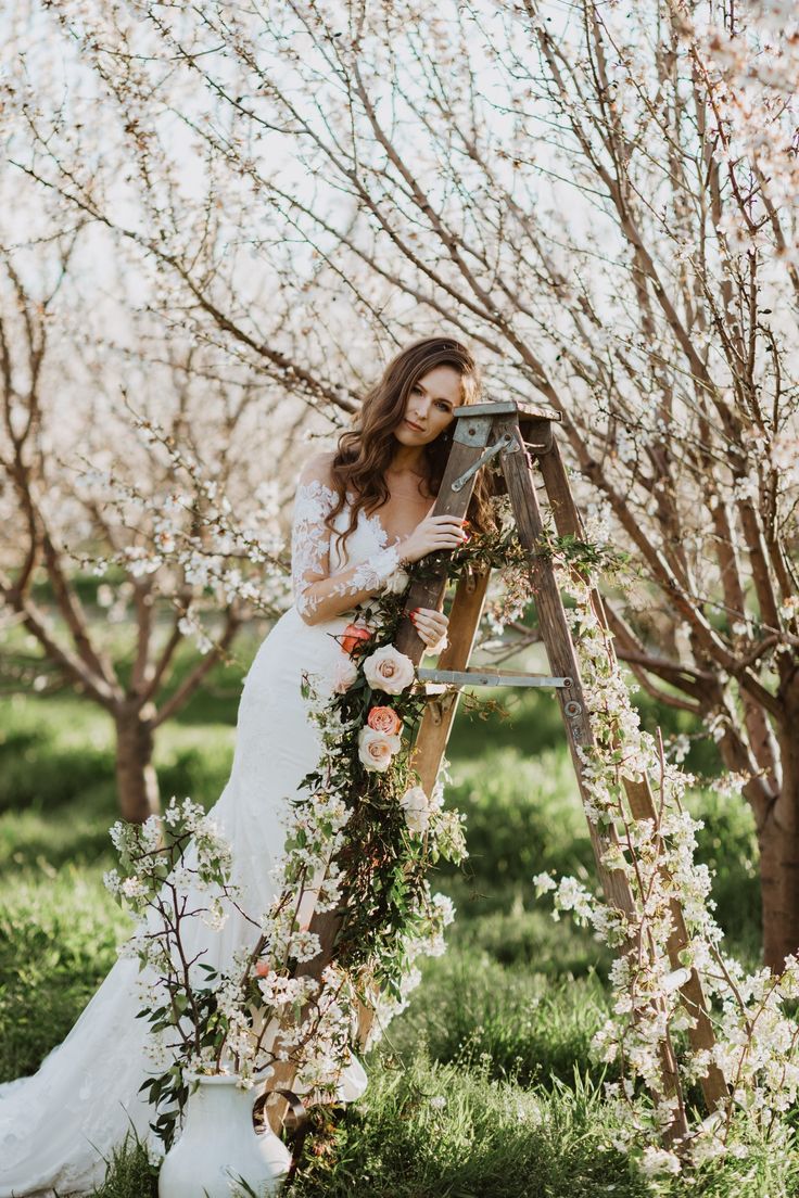 a woman in a wedding dress standing next to a ladder with flowers and greenery on it