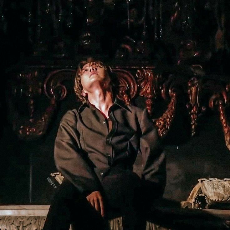 a man sitting on top of a wooden bench next to an ornate headboard in a dark room