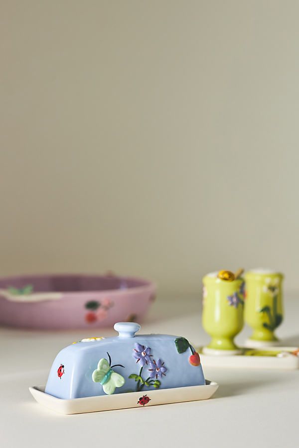 a small blue covered dish sitting on top of a table next to two yellow cups