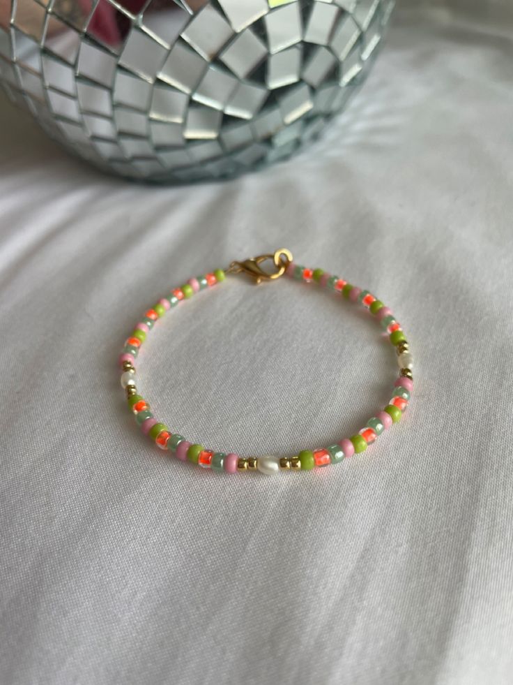 a beaded bracelet sitting on top of a bed next to a bowl of fruit