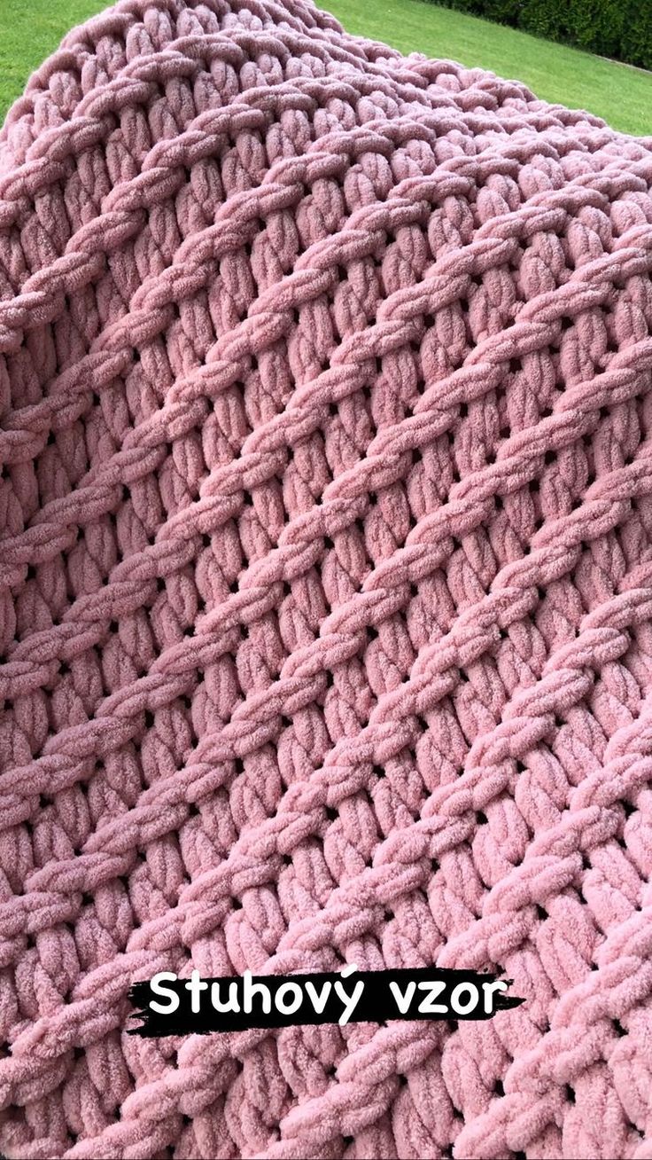 a pink crocheted blanket sitting on top of a grass covered field