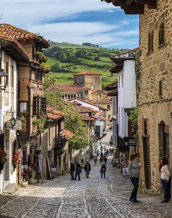 people are walking down an old cobblestone street in the mountainside town center