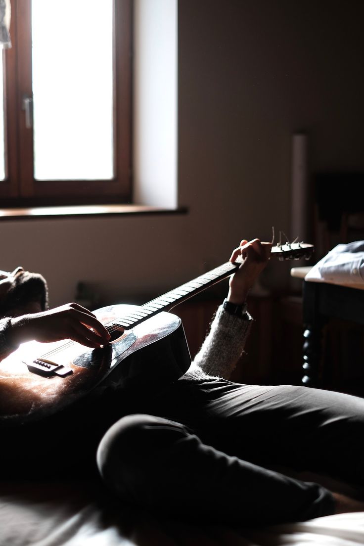 a man sitting on top of a bed holding a guitar