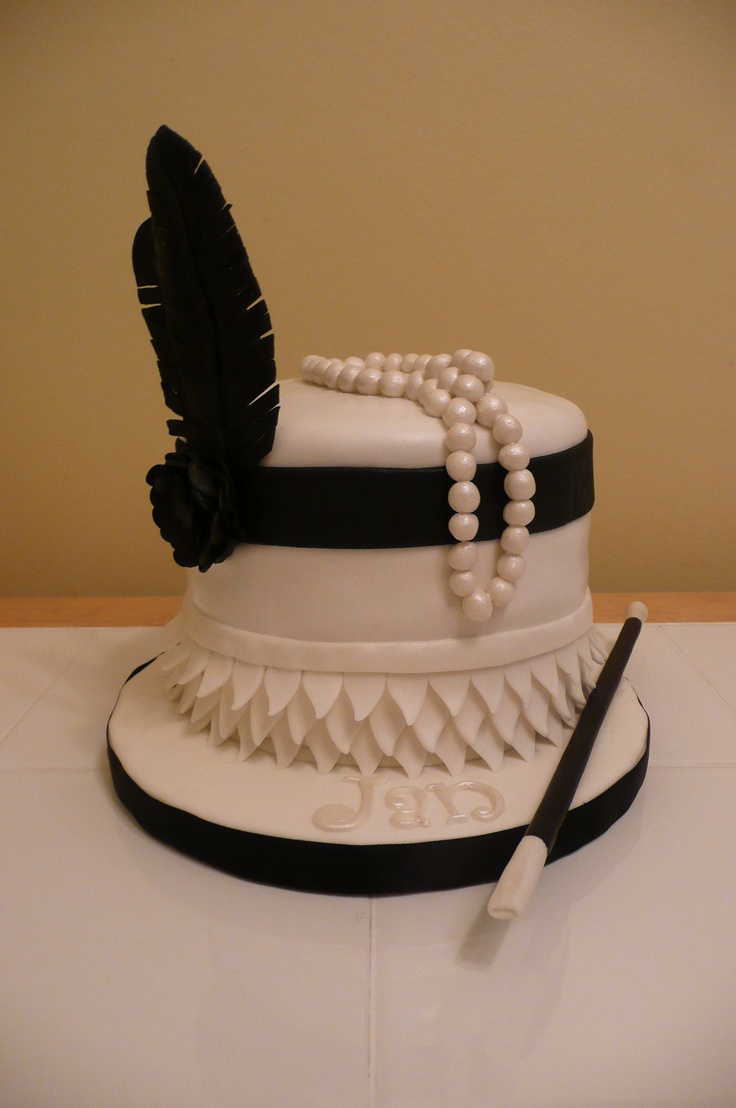 a wedding cake decorated with pearls, feathers and beads on a table next to a pen