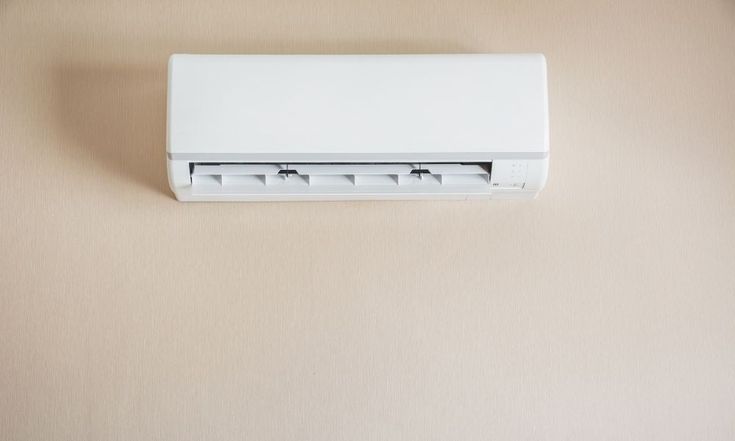 a wall mounted air conditioner sitting on top of a beige wall next to a window