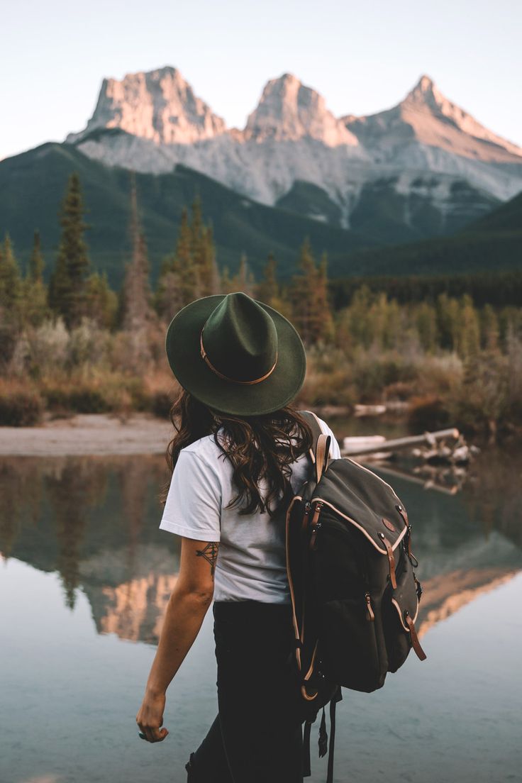 a person with a hat and backpack walking by the water in front of some mountains