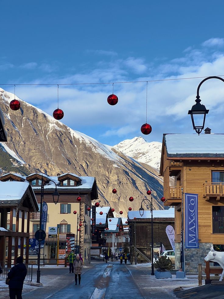 a town with mountains in the background and people walking down the street under red lanterns