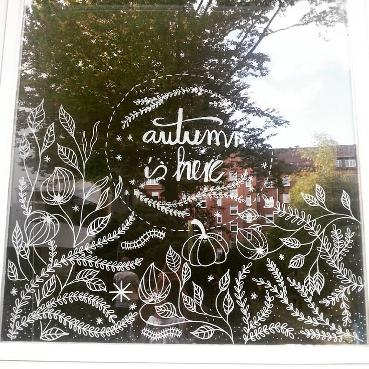 a window with the words autumn is here drawn on it in front of some trees