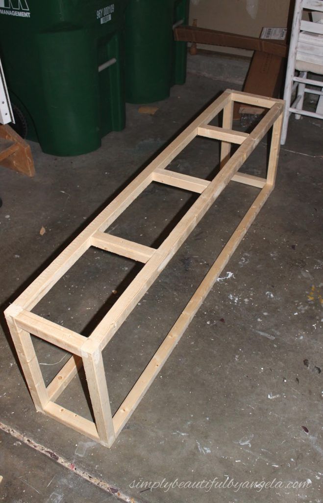 a wooden bench sitting on top of a floor next to green trash cans and barrels