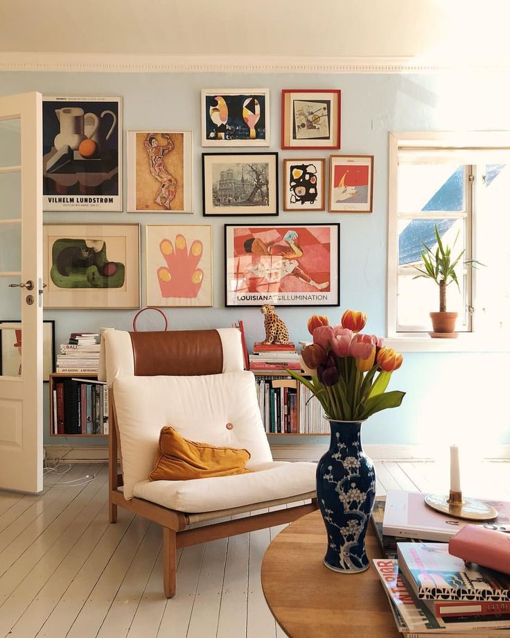 a living room with pictures on the wall and a chair next to a vase filled with flowers