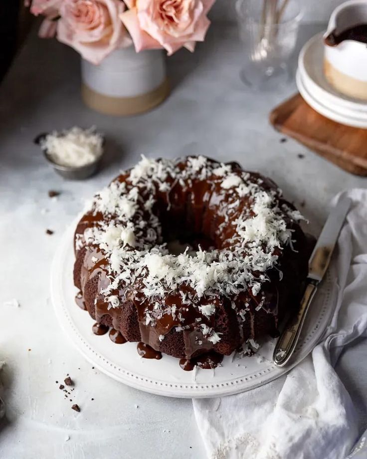 a chocolate bundt cake sitting on top of a white plate next to pink flowers