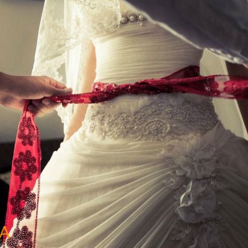 the bride is getting ready to put on her wedding dress and tie it with a red ribbon