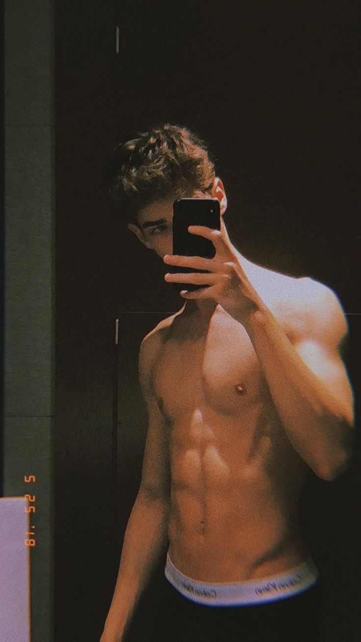 a shirtless man taking a selfie in front of a mirror with his cell phone