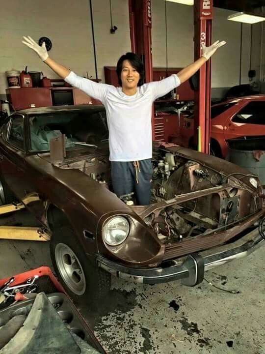 a man standing on the hood of a car in a garage with his arms outstretched