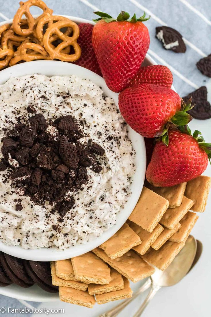 a bowl of dip surrounded by crackers, strawberries and pretzels on a platter