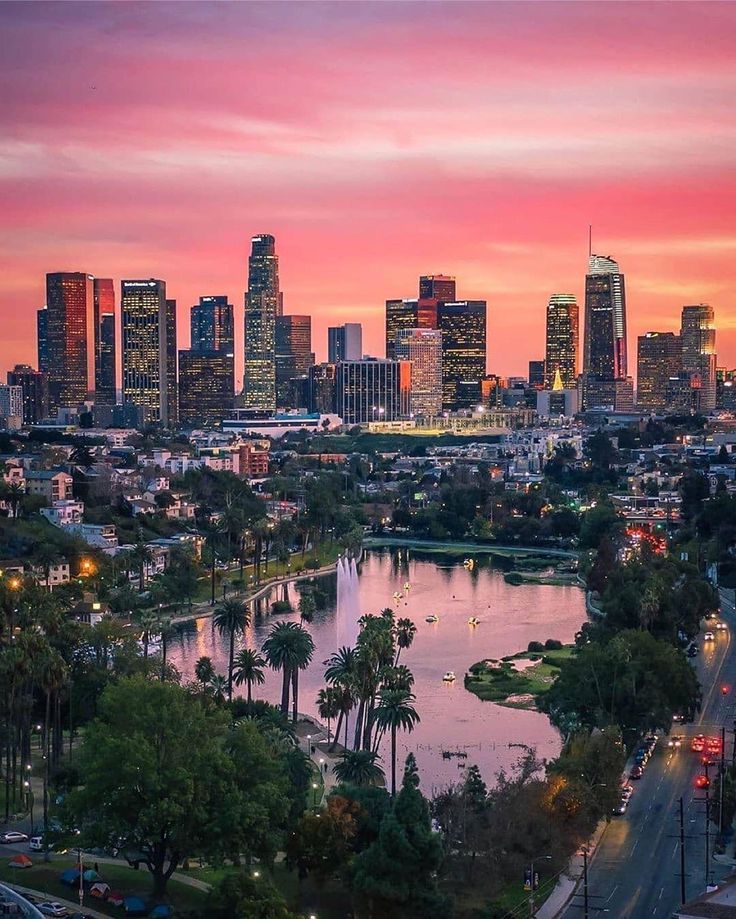 the city skyline is lit up at sunset with pink clouds in the sky and palm trees