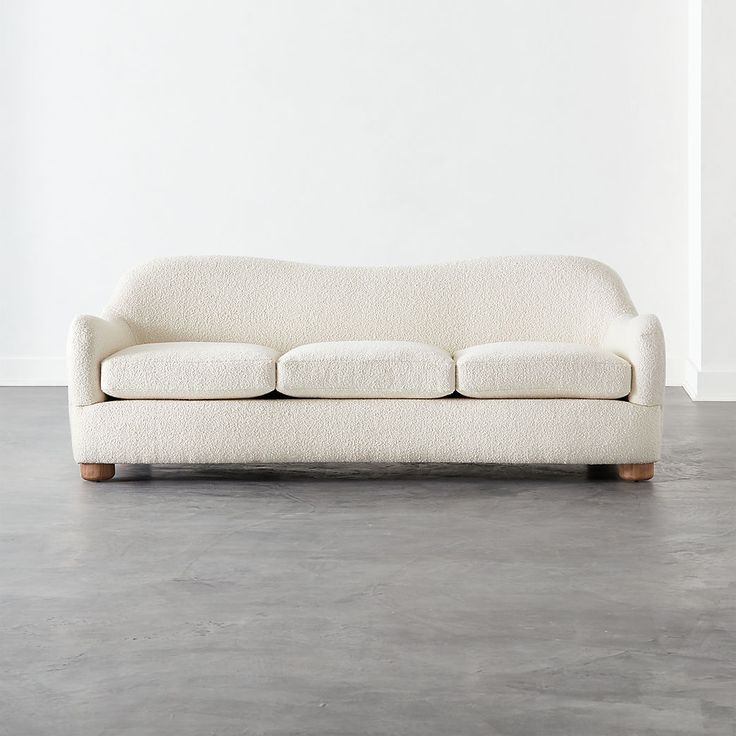 a white couch sitting on top of a cement floor next to a wall and window