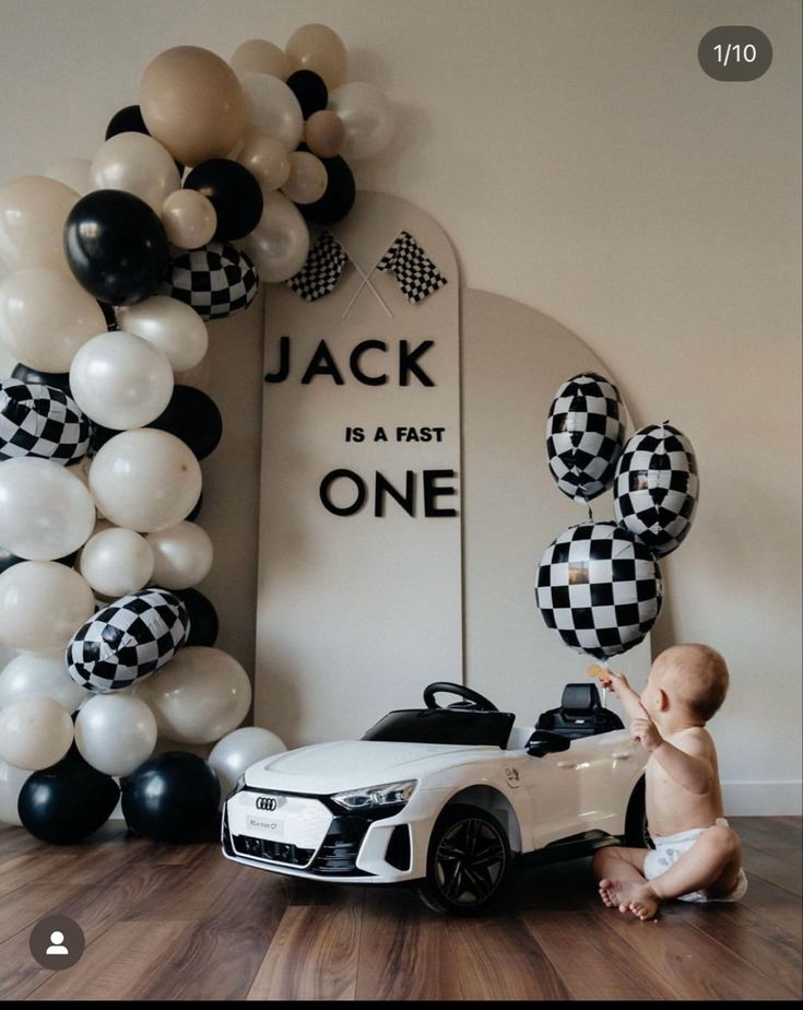 a baby is playing with a toy car in front of balloons and a sign that says jack is a fast one