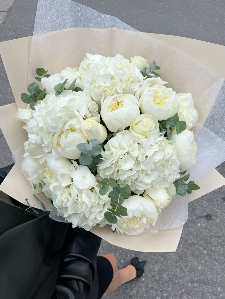 a bouquet of white flowers sitting on top of a paper wrapper next to a sidewalk