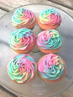 six cupcakes with colorful frosting on a glass plate sitting on a wooden table