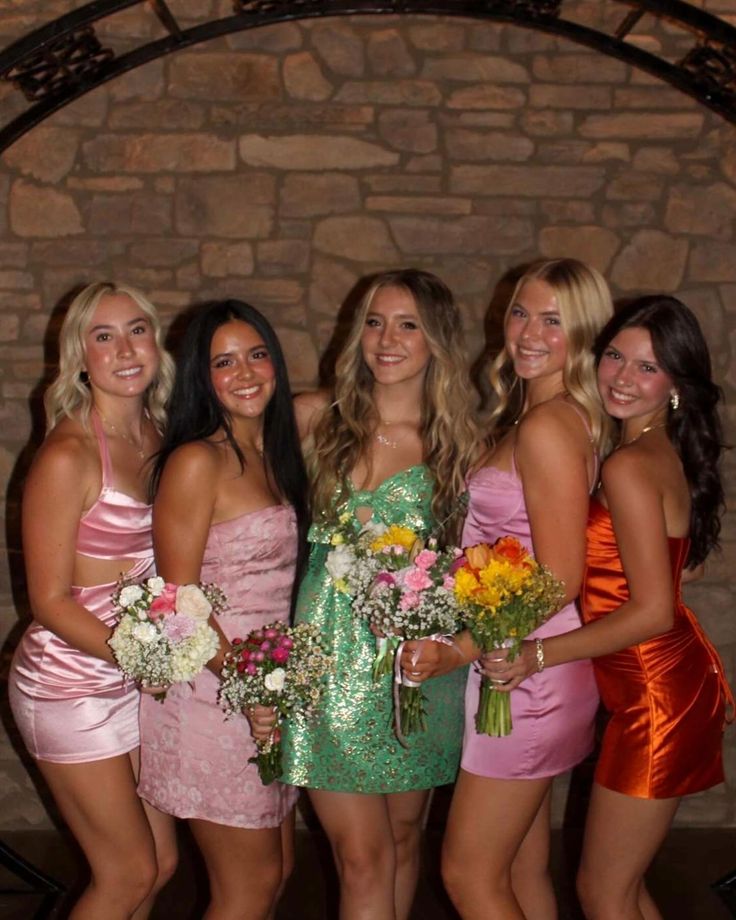 a group of women standing next to each other in short dresses and holding bouquets