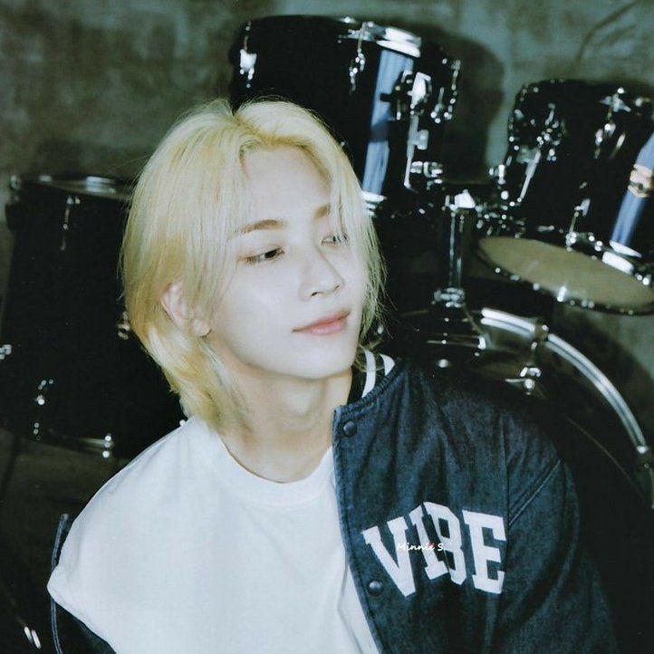 a person with blonde hair sitting in front of a drum set and looking at the camera