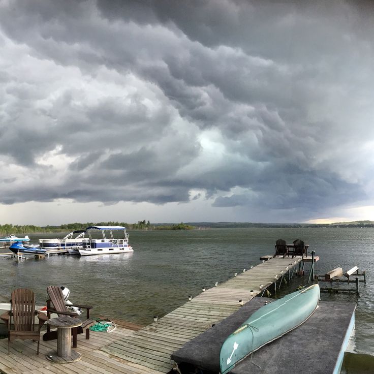 boats are docked at the end of a dock on a lake under a cloudy sky