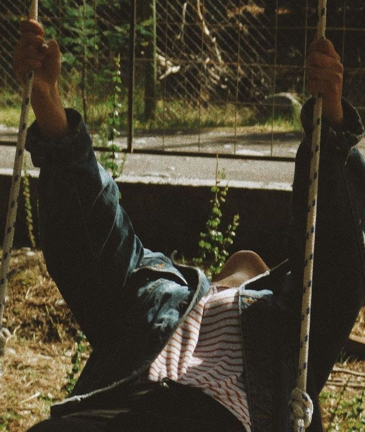 a person sitting on a swing with their feet in the air and one hand up