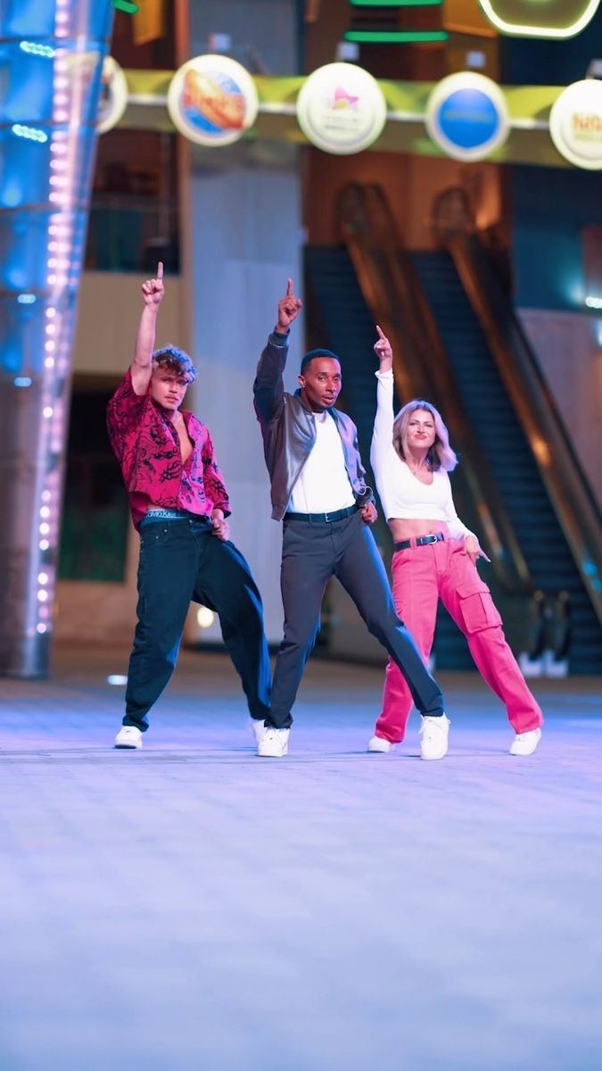 three young people are dancing in front of a building with lights and signs above them