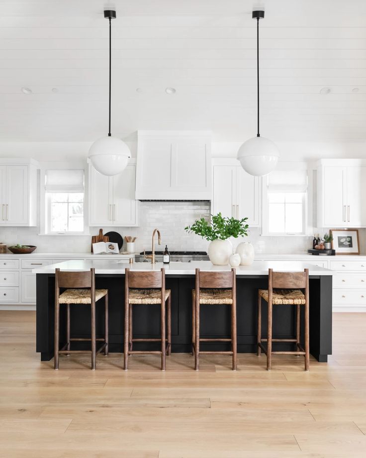 a kitchen with white cabinets and black island in the center is surrounded by stools