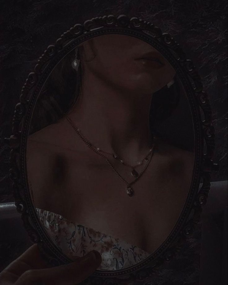 a woman is looking at herself in the mirror with her hand on her chest and wearing a necklace