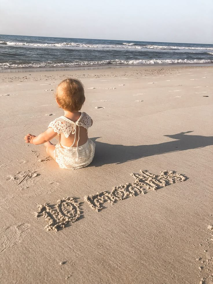 a baby sitting in the sand at the beach and writing it's name into the sand