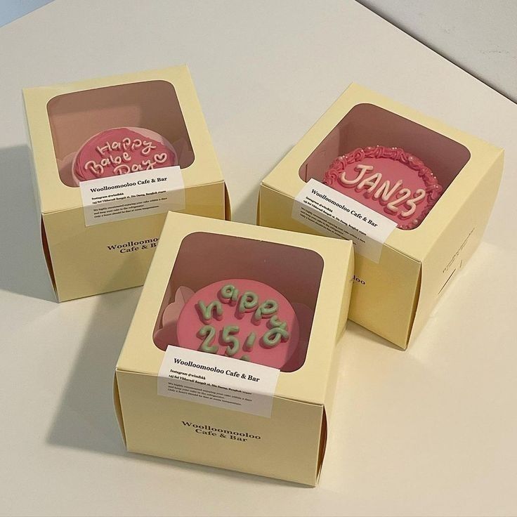 three pink cupcakes in boxes with happy birthday written on the top and bottom