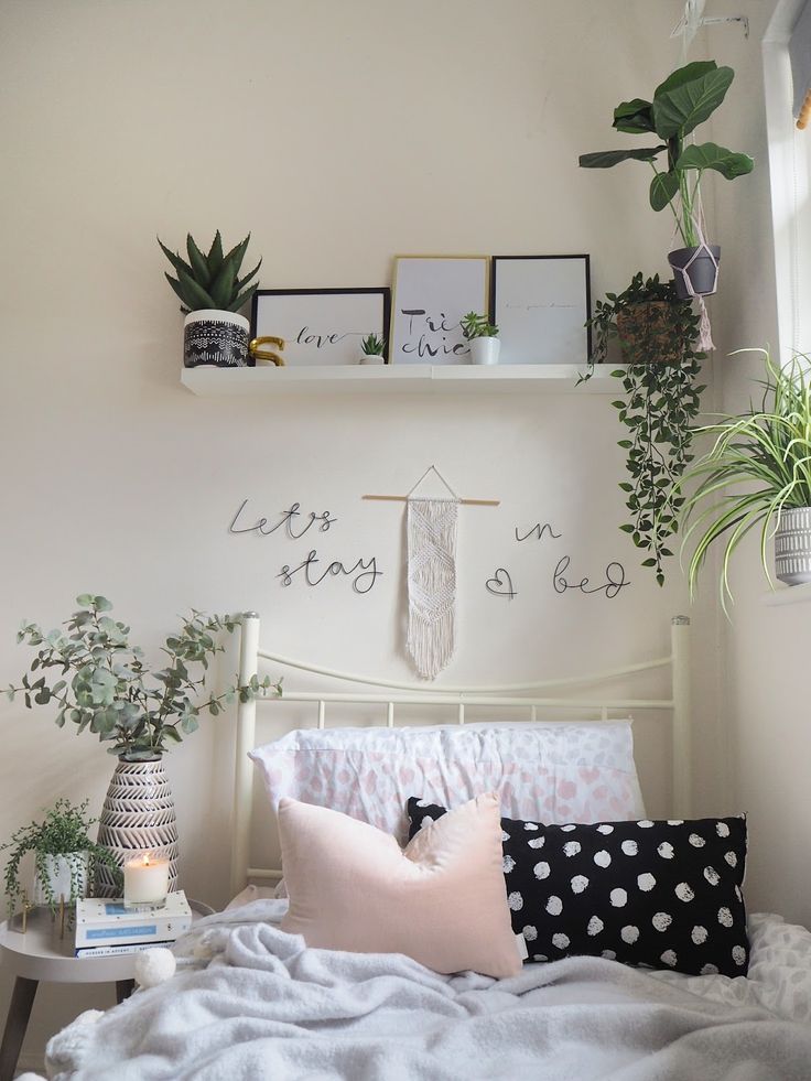 a white bed topped with lots of pillows next to a shelf filled with potted plants