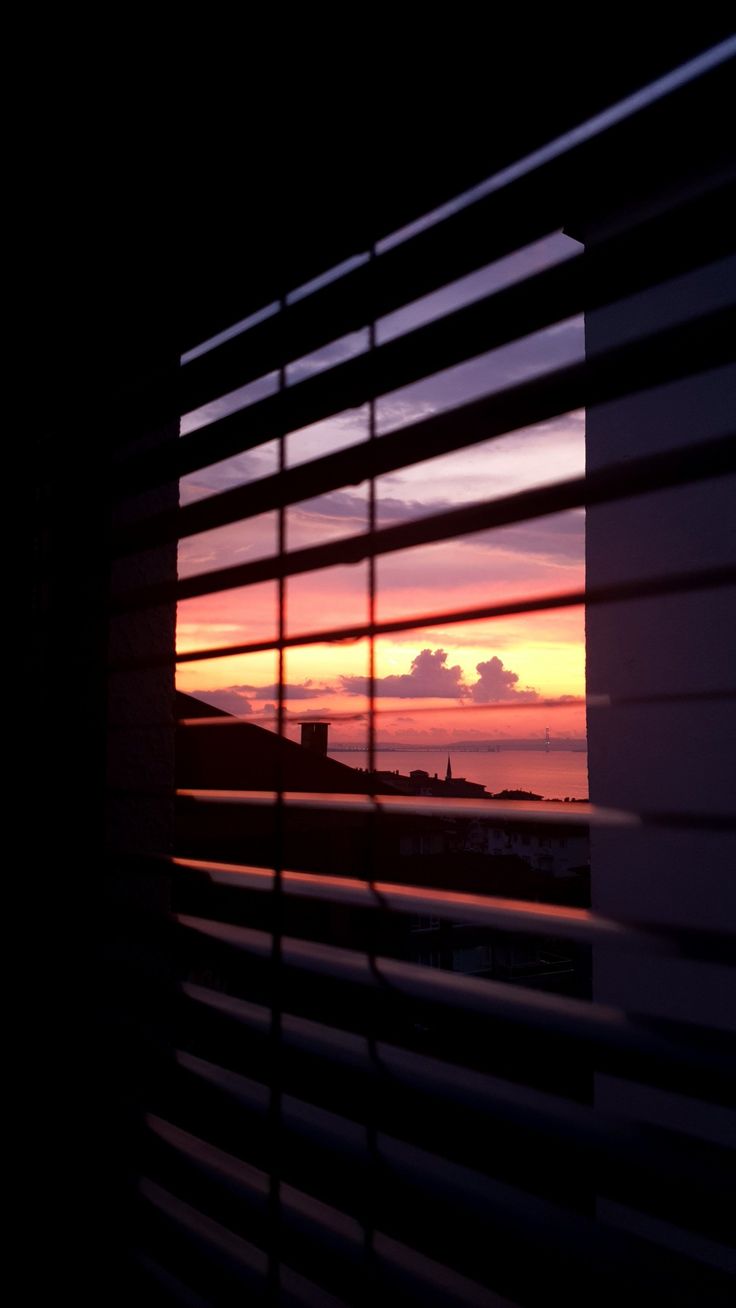 the sun is setting behind some blinds