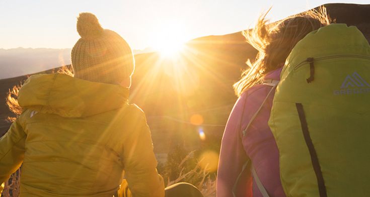 three people standing on top of a mountain with the sun shining behind them and mountains in the background