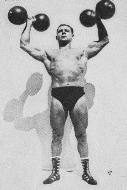 a man with no shirt holding two balls in front of his head and shoulders while standing on one leg