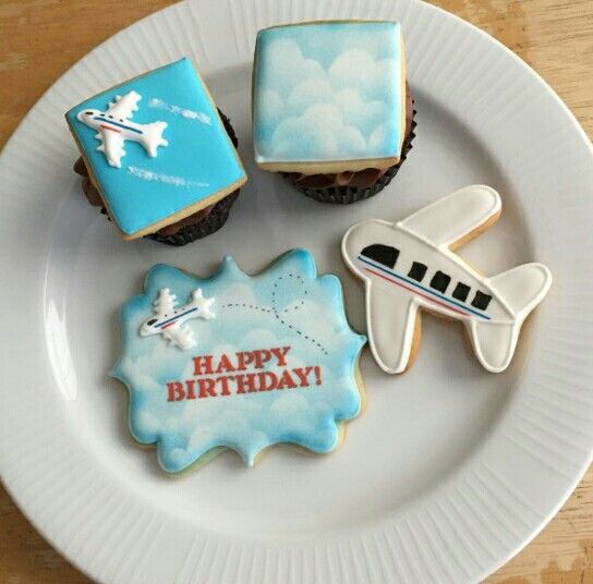 three decorated cookies sitting on top of a white plate next to an airplane and plane cookie