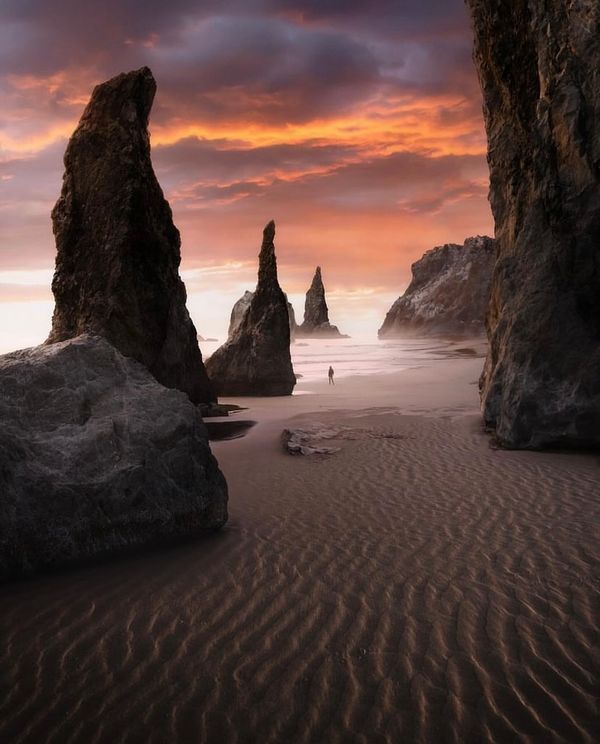 a person is walking on the beach near some rocks and water at sunset or dawn