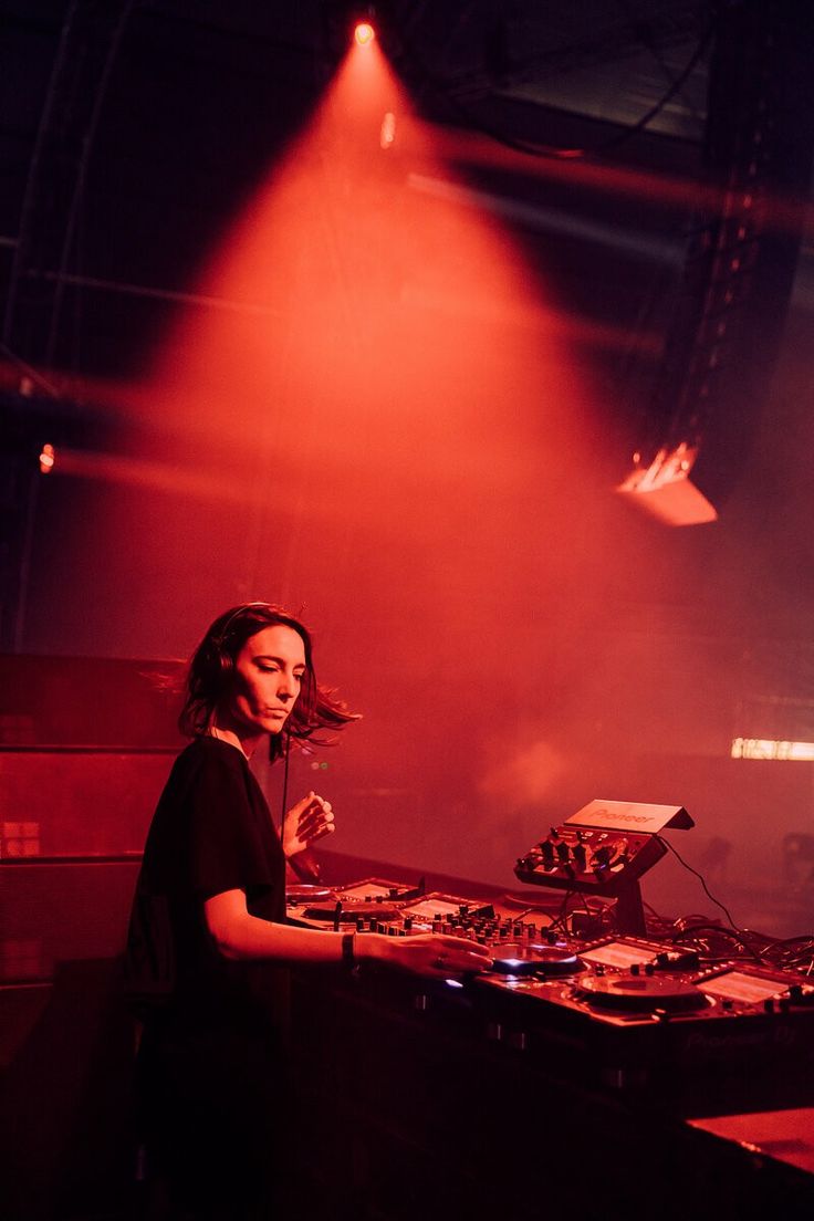 a woman standing in front of a dj's equipment set up on a stage