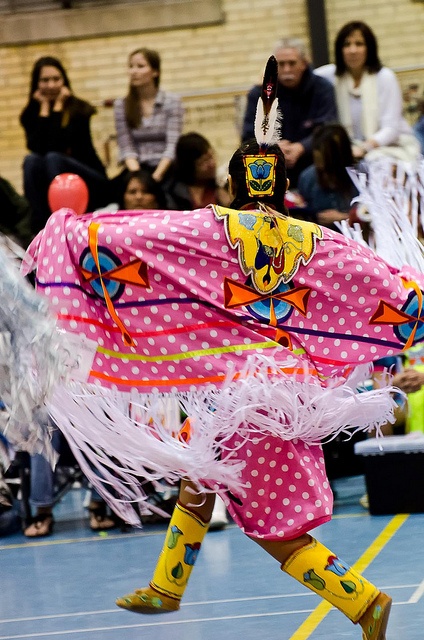 a woman in pink and white costume with feathers on her head walking across a basketball court