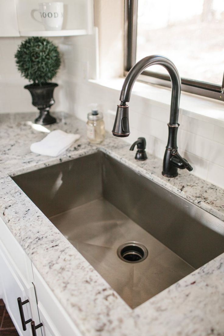 a kitchen sink under a window next to a counter top with a potted plant